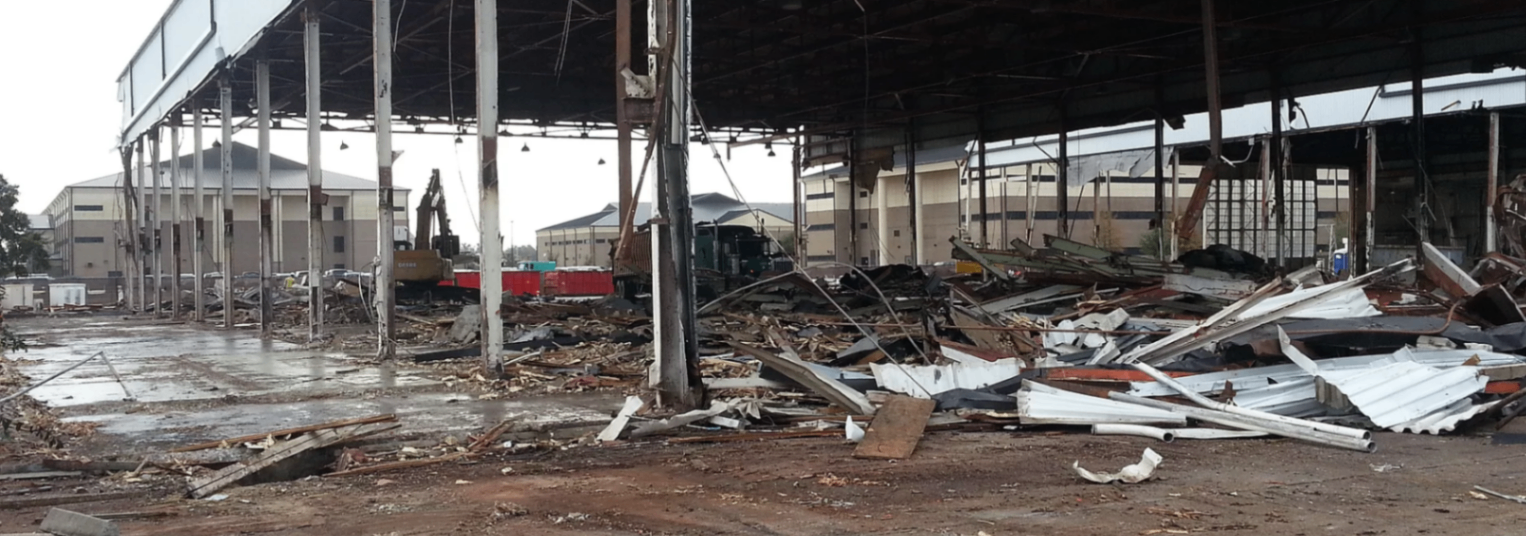 Partially demolished industrial building with exposed steel framing and concrete debris being cleared by CW Mobile Service crew